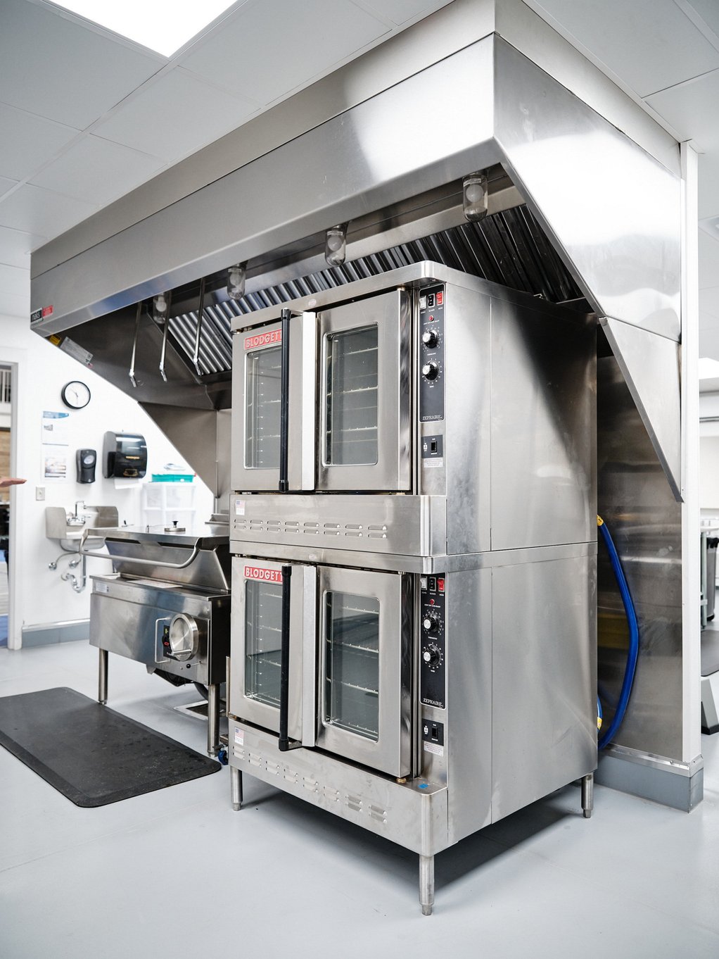 A double deck convection oven and commercial tilt skillet are installed beneath a large hood