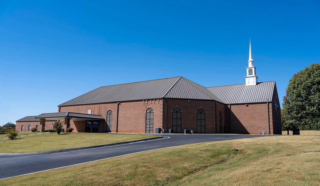 A red brick building with a white spire sits on a field of short grass framed by the bright blue sky